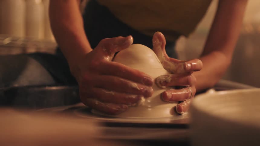 Hands shaping wet clay on spinning pottery wheel in cozy setting