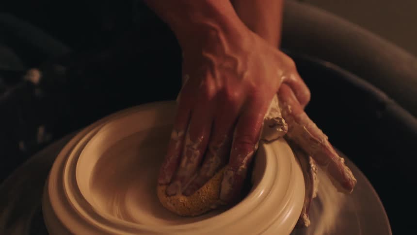 Female hands molding clay on a wheel indoors
