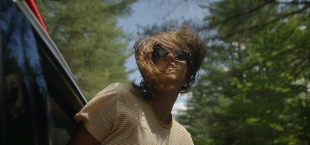 A woman sticks her head out the passenger window of a moving car