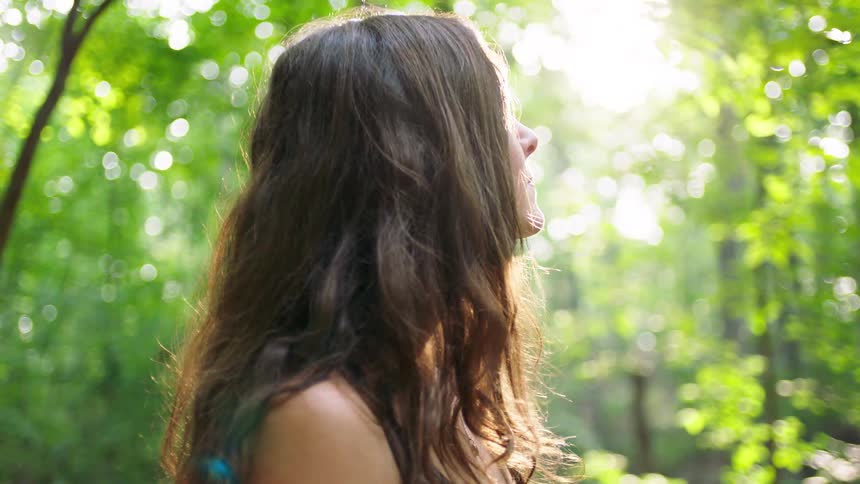 Woman seen in profile in a wooded area with natural light filtering through the trees