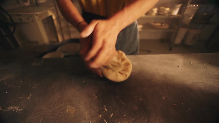 In the warm ambiance of a studio a potter firmly kneads and spirals a lump of clay on a workbench her hands rhythmically pressing the material to remove air bubbles