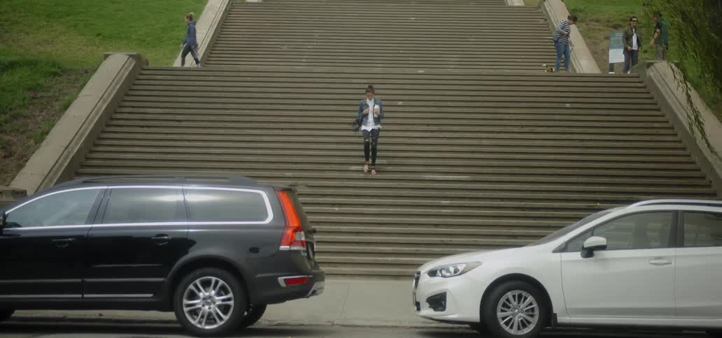 A woman walking down a wide and long set of steps outside as cars drive by