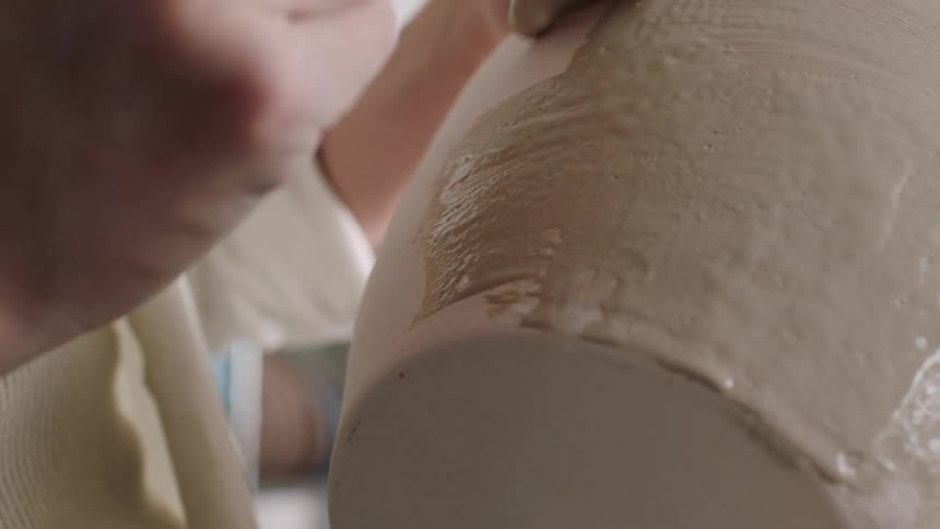 Brush applies coating to an unfired ceramic piece during the finishing process