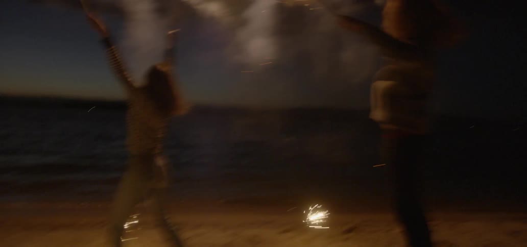 Women jump with fireworks on a beach