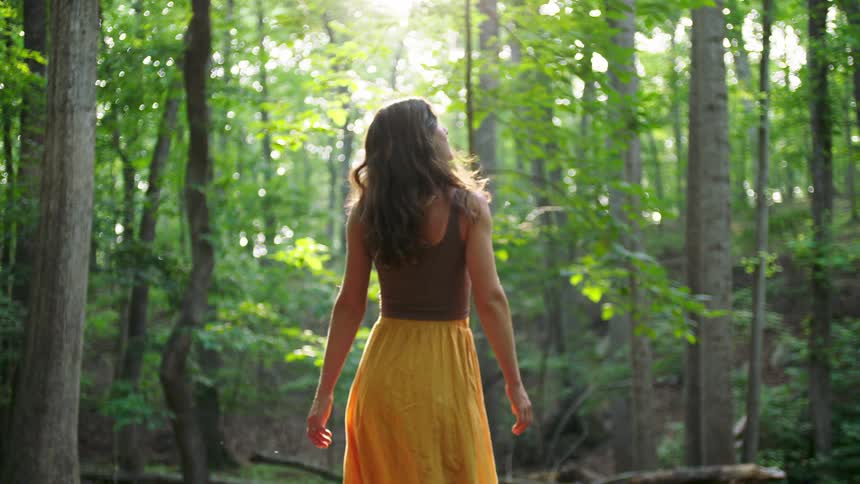 Woman looks around while walking in the woods on a sunny summer day