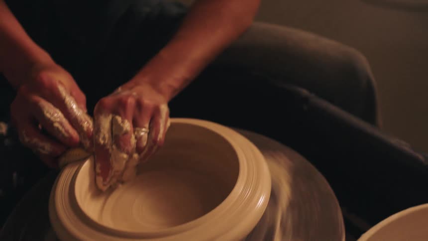 Young adult woman molding clay on a wheel indoors