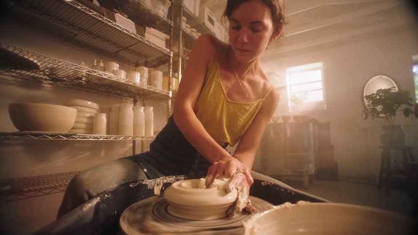 Female potter shapes a bowl turning on a pottery wheel during the daytime