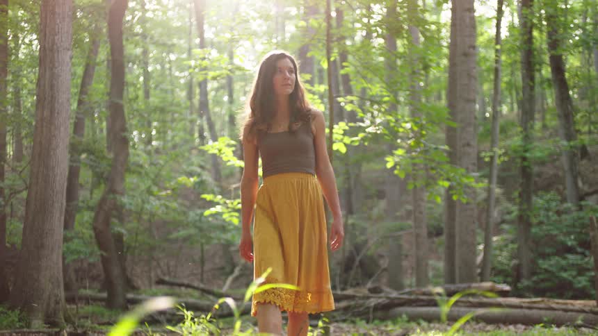 Young woman wearing a long skirt looks around as she walks out of the woods
