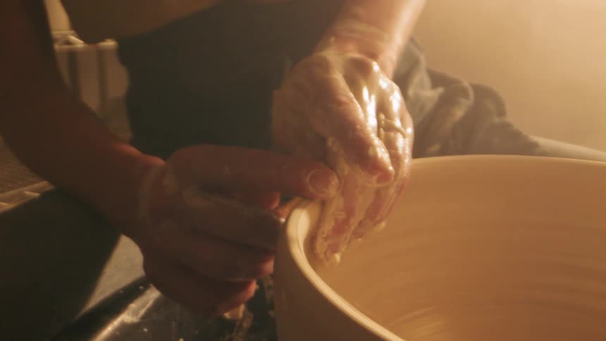 Claycovered hands shape the rim of a ceramic piece on a pottery wheel