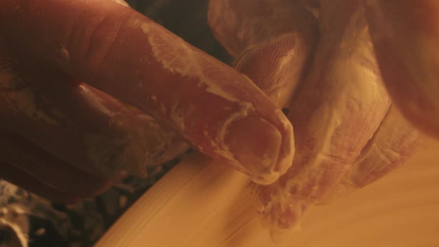 Claycovered hands shaping pot on pottery wheel under warm light in artistic setting
