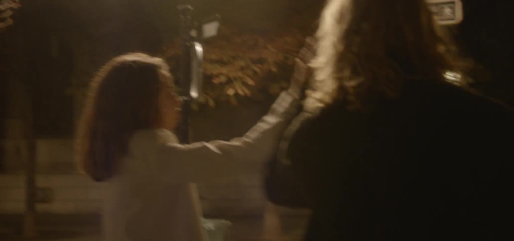 A man and woman walk on a city sidewalk at night