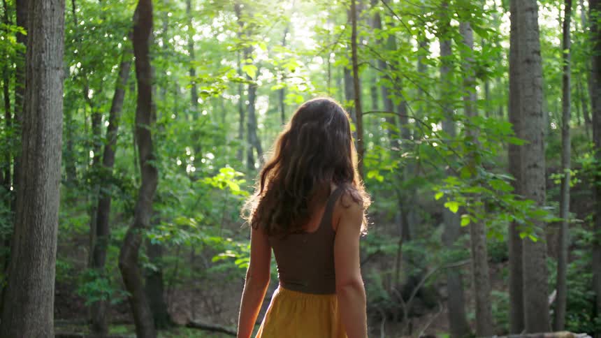 Woman looks around while walking in the woods on a summer day