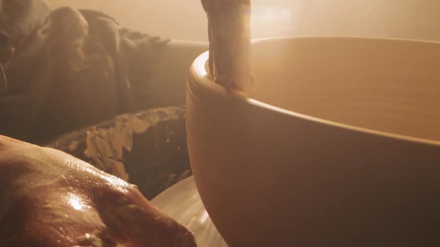 Human hands molding clay on a wheel using a sponge indoors