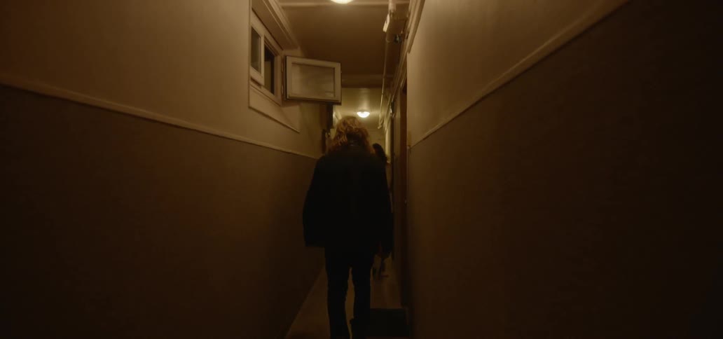 A man and a woman walk down a long narrow hallway