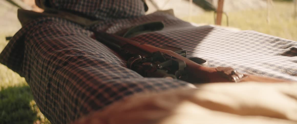 Rifle lies on a cot in camp on a sunny day