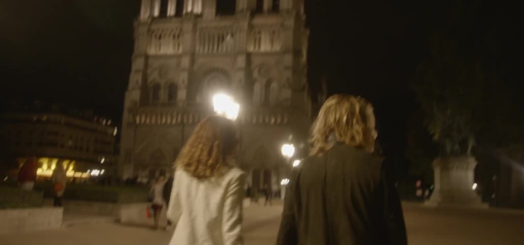 A man and woman hold hands while walking in a city at night