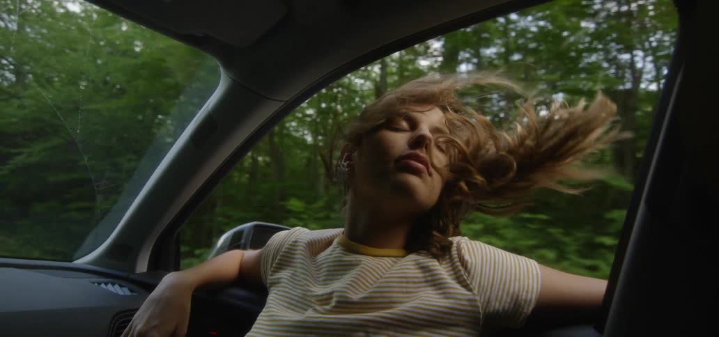 A woman hangs her head from the window of a moving car