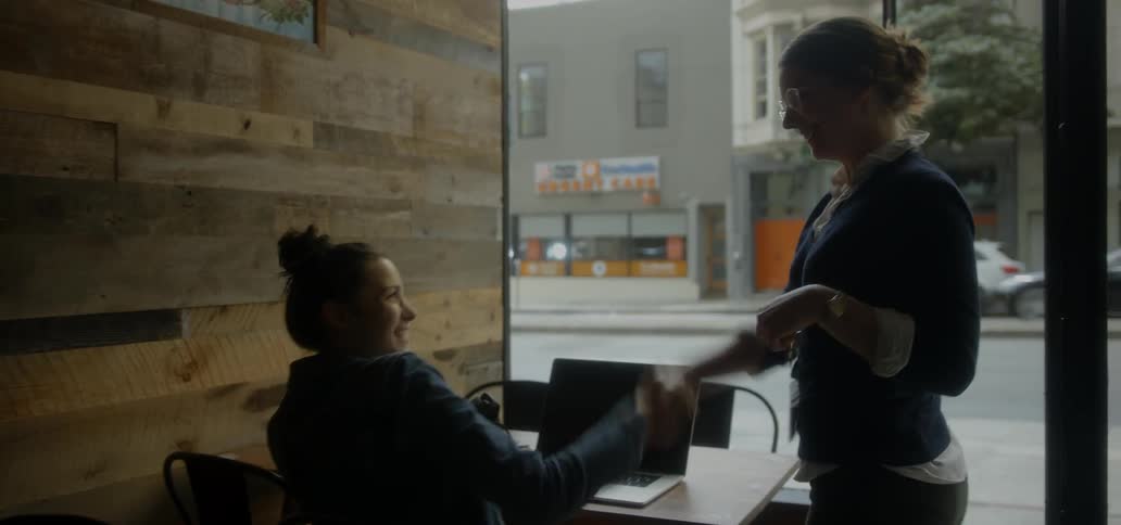 Two women shake hands and sit at a table together