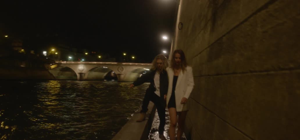 A man and woman walk on a narrow path next to a river