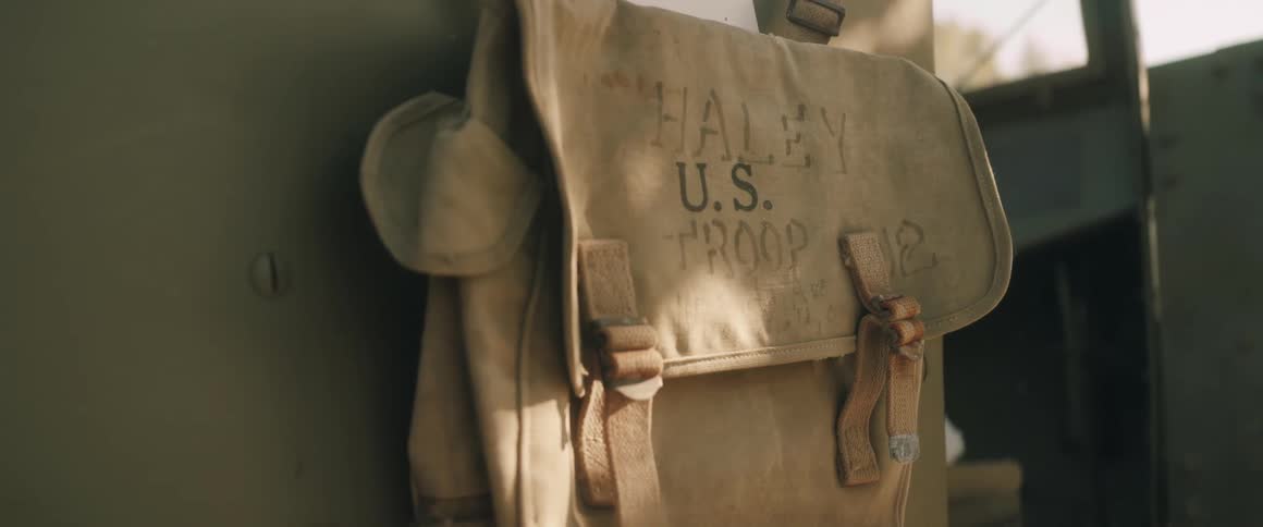 A static closeup shot of a worn tan canvas militarystyle bag inside a vehicle secured by brown leather straps and hanging against a green surface
