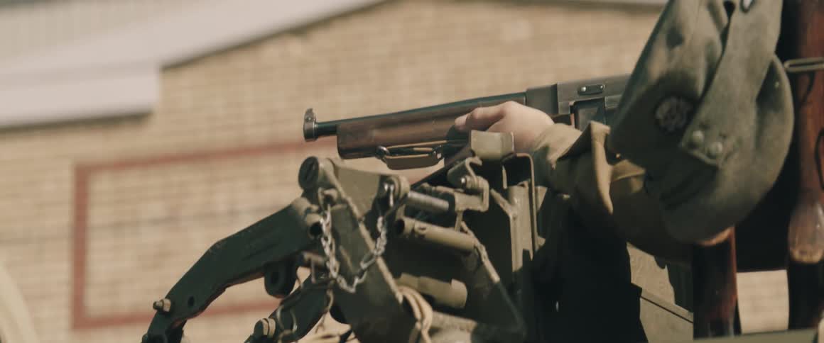 A military officer standing on a military vehicle firing his weapn at midday