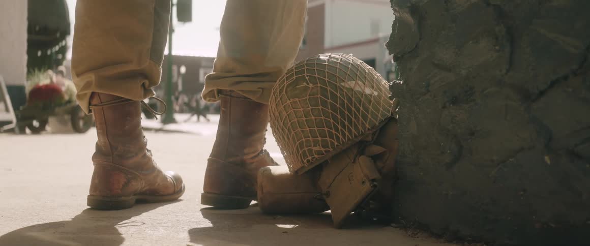 Soldier with leather boots and khaki pants beside helmet and pouches in historical urban scene