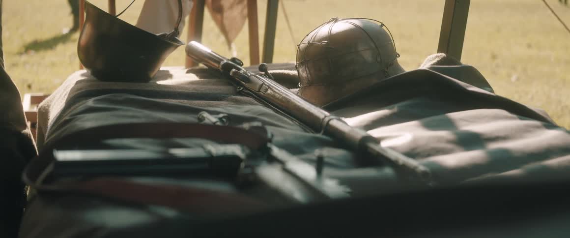 Boltaction rifle and vintage military helmets on blanket in sunlit grassy area