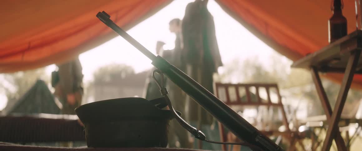 Rifle leans near a helmet in a military tent during the daytime