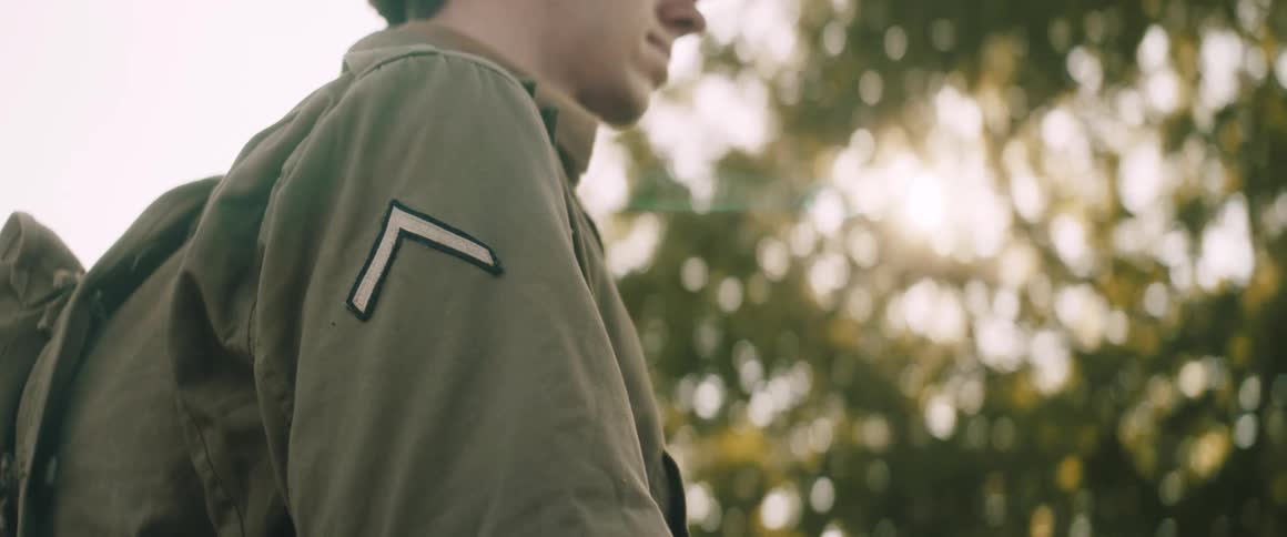 A young soldier stands in profile the setting sun glinting off the patch on his vintage army jacket
