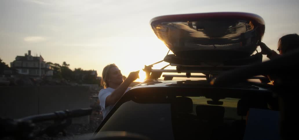 A man unties something from the top of his car