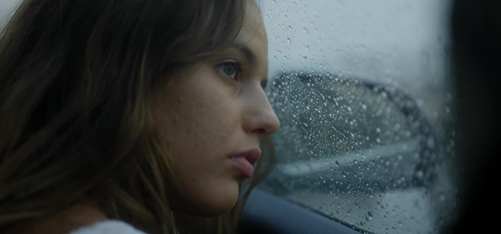 A woman looks out a car window during a rainstorm
