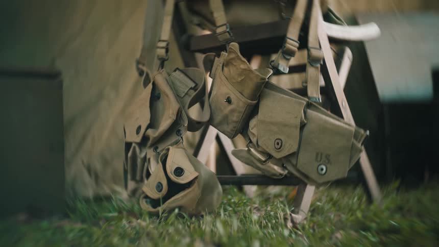 Military backpack with pouches and straps resting on grass beside a tent