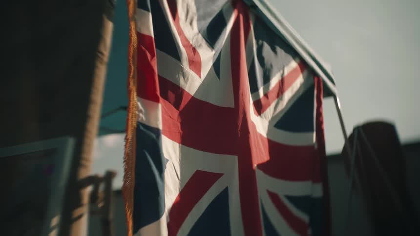 A union jack or united kingdom flag hangs outdoors on a pole with a dark blurred background under a bright overcast sky