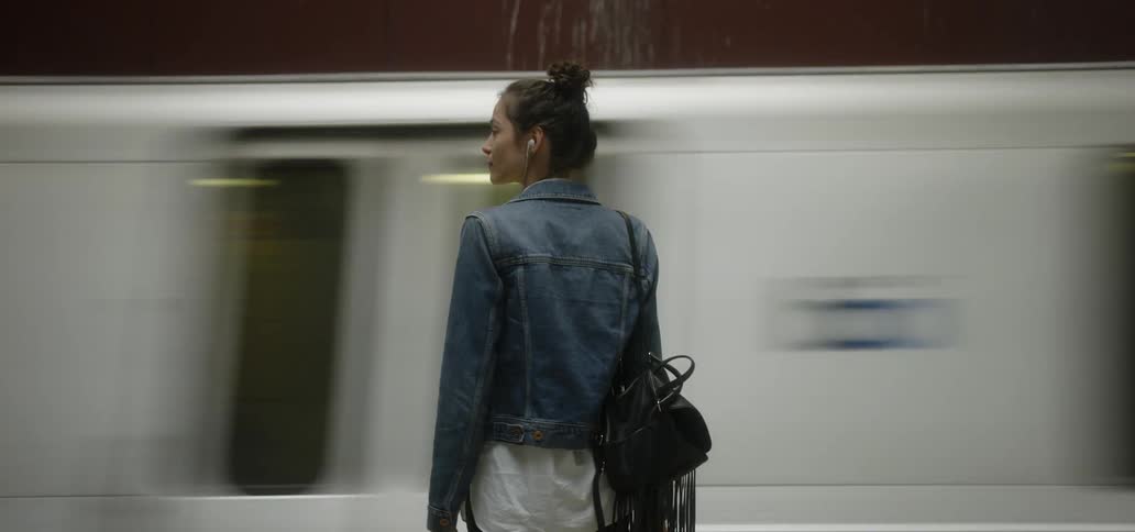 A woman stands in front of a moving subway train