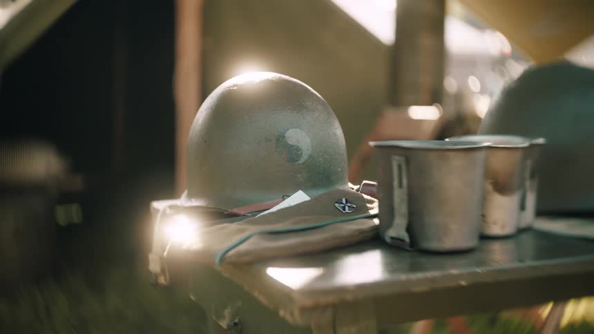 Military helmet with circular insignia beside folded uniform and canteens on wooden table