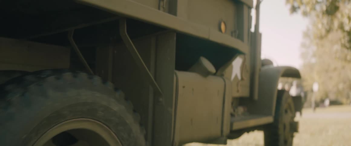Side section of a military truck parked outdoors with compartments and a visible wheel