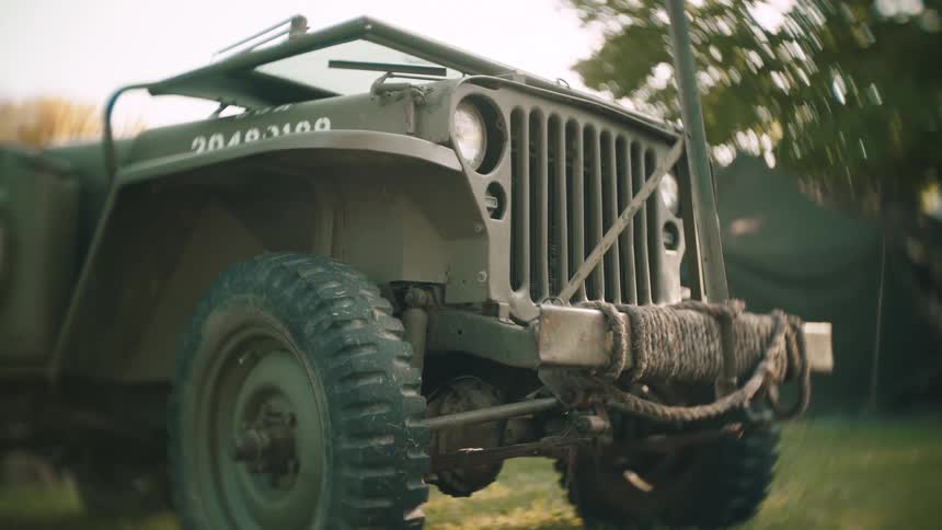 Military jeep parked outside near a tent and trees
