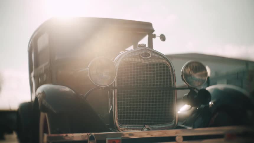 The exterior of an old green car with headlights on the front and sunlight illuminating its surface