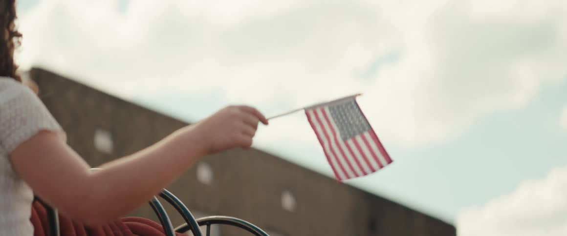 Hand holding united states flag above red hose coiled on metal reel