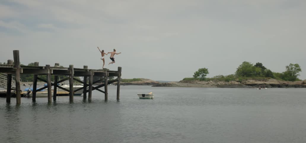 Man and woman run and hold hands and jump off a dock