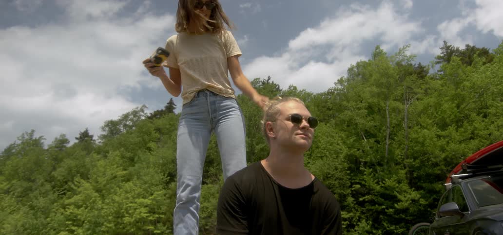 Woman stands above a man and takes a picture of nature