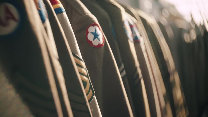 Some military uniforms on hangers with various symbols on the arm