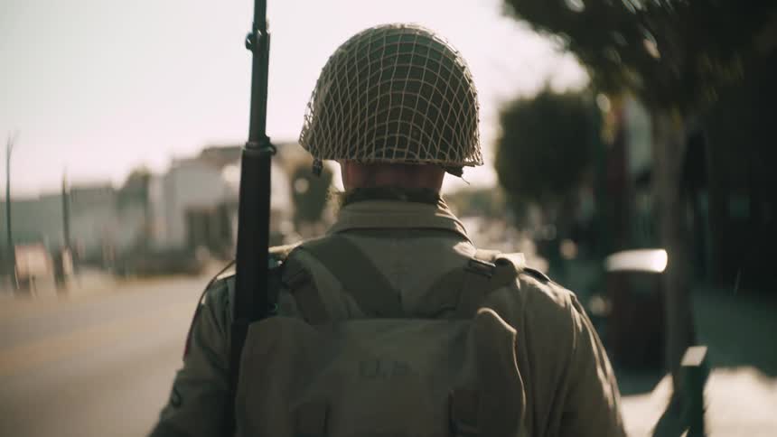 Military soldier walking outside of buildings with a rifle over his shoulder