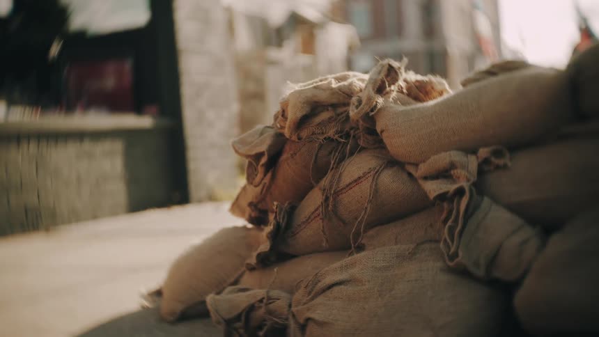 A pile of tied burlap bags sit on a sidewalk near houses