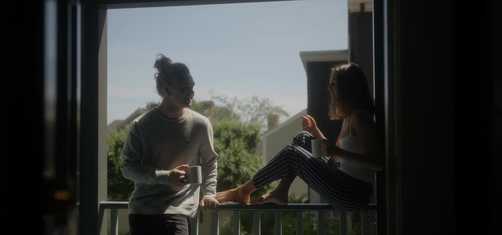 A man and woman drink coffee on a porch on a sunny day