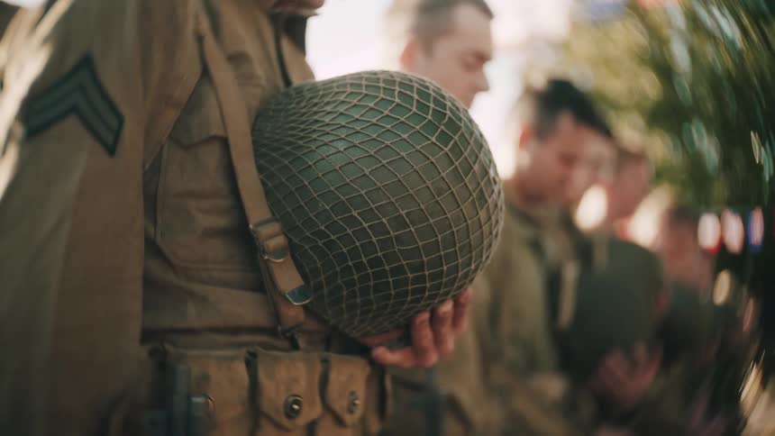 Soldier holds a military helmet while other service members stand aligned in an outdoor setting