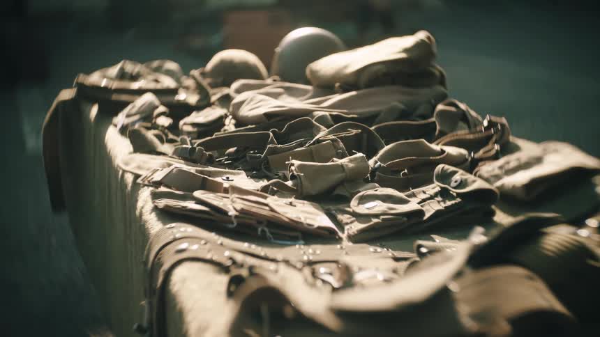 An assortment of vintage military equipment including helmets and webbing is laid out across a table the gear is primarily olive drab and tan presented in a closeup shot with a soft blurred background