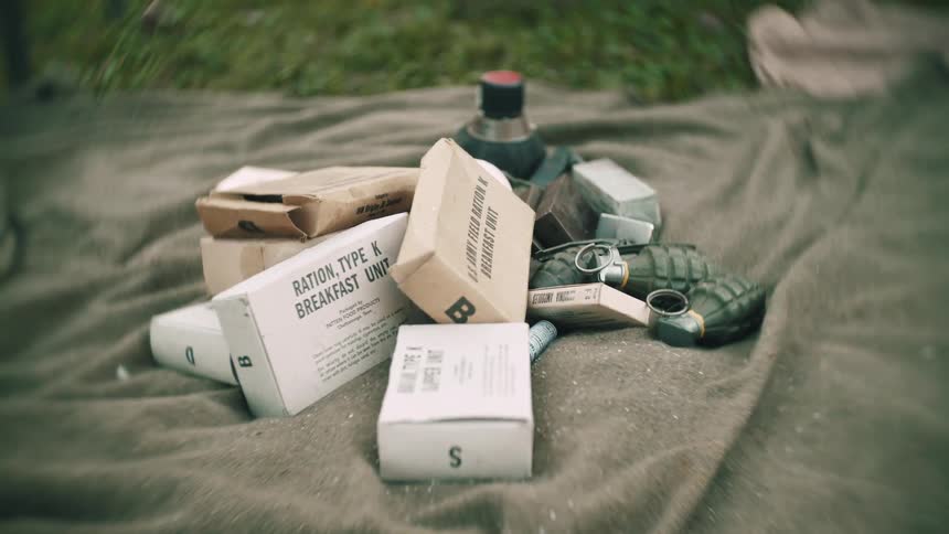 Military meal rations in small boxes on a blanket with hand grenades