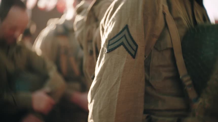 Rank insignia stitched on the sleeve of a military uniform with soldiers in the background