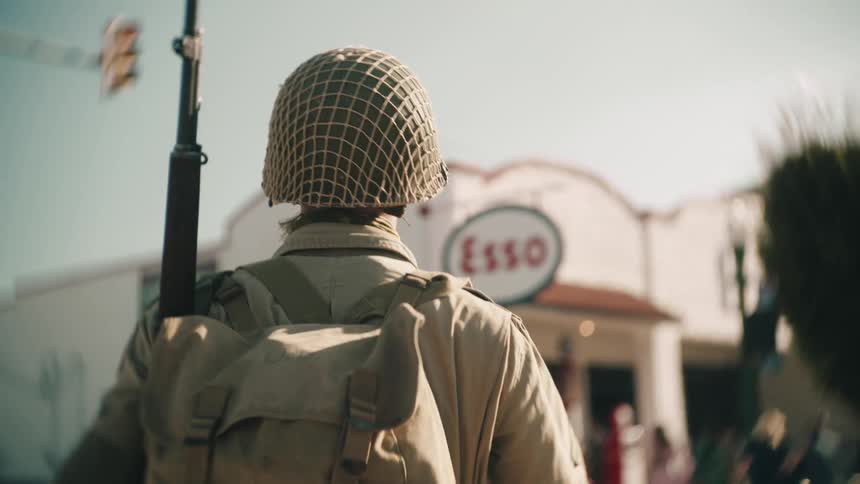 Soldier carrying a rifle walks through an intersection on a sunny day